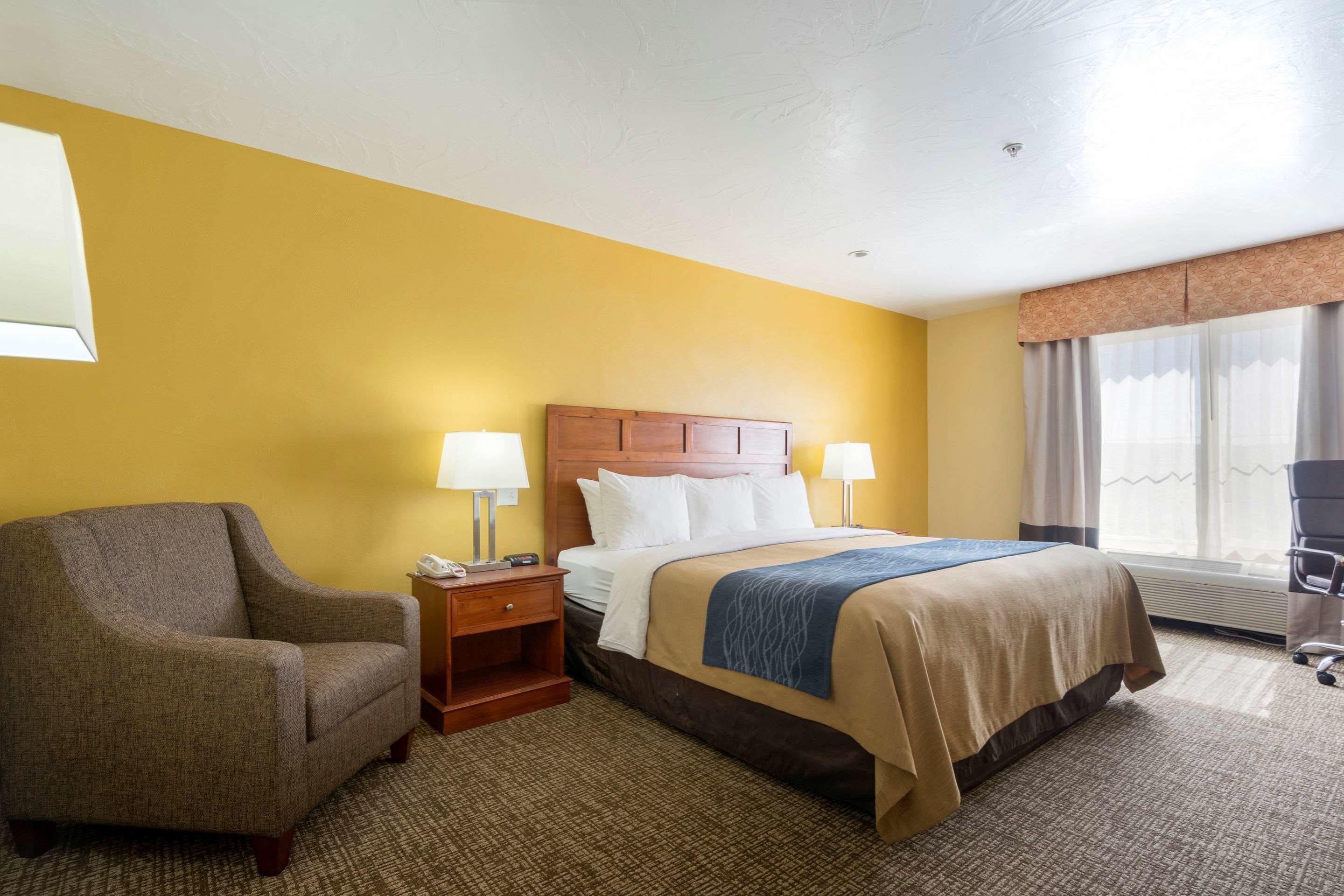 A hotel room with a large bed, a chair, a nightstand, and a window with curtains.