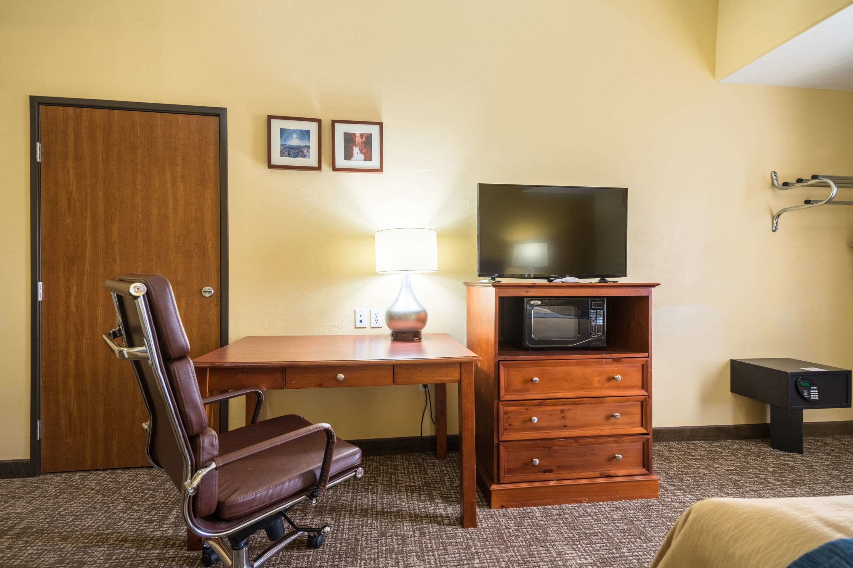 A hotel room with a wooden desk, a leather chair, a television, a lamp, a microwave, and a safe.