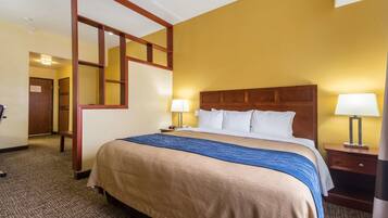 A hotel room with a large bed, wooden headboard, two bedside tables with lamps, a carpeted floor, and a door leading to another room.