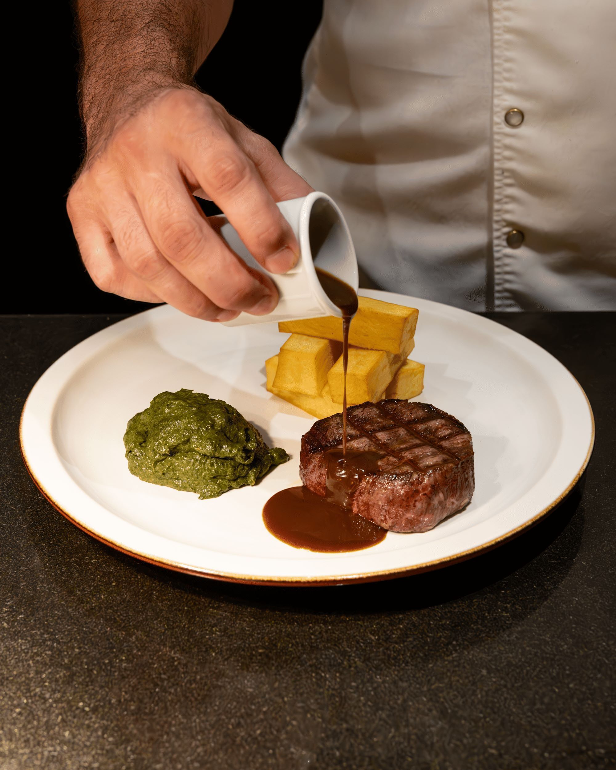 Un plato con bistecca, puré de papas y salsa verde.