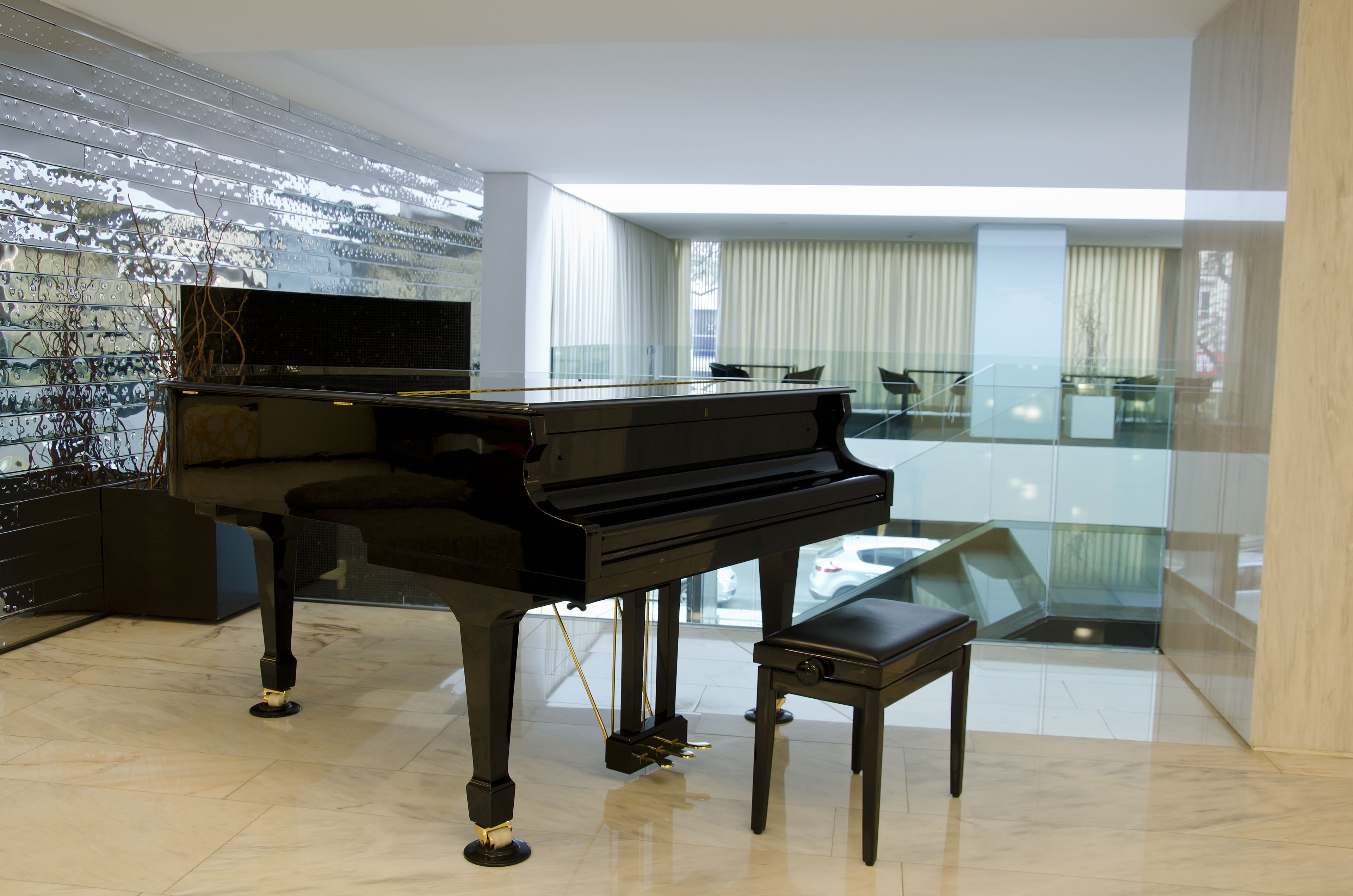 A grand piano in a spacious, modern living room with a high ceiling and large windows.