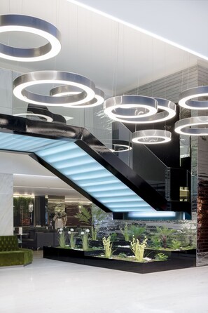 A modern lobby with a glass staircase, circular ceiling lights, and indoor plants. - VIP Grand Lisboa Hotel & Spa (Lisbon)