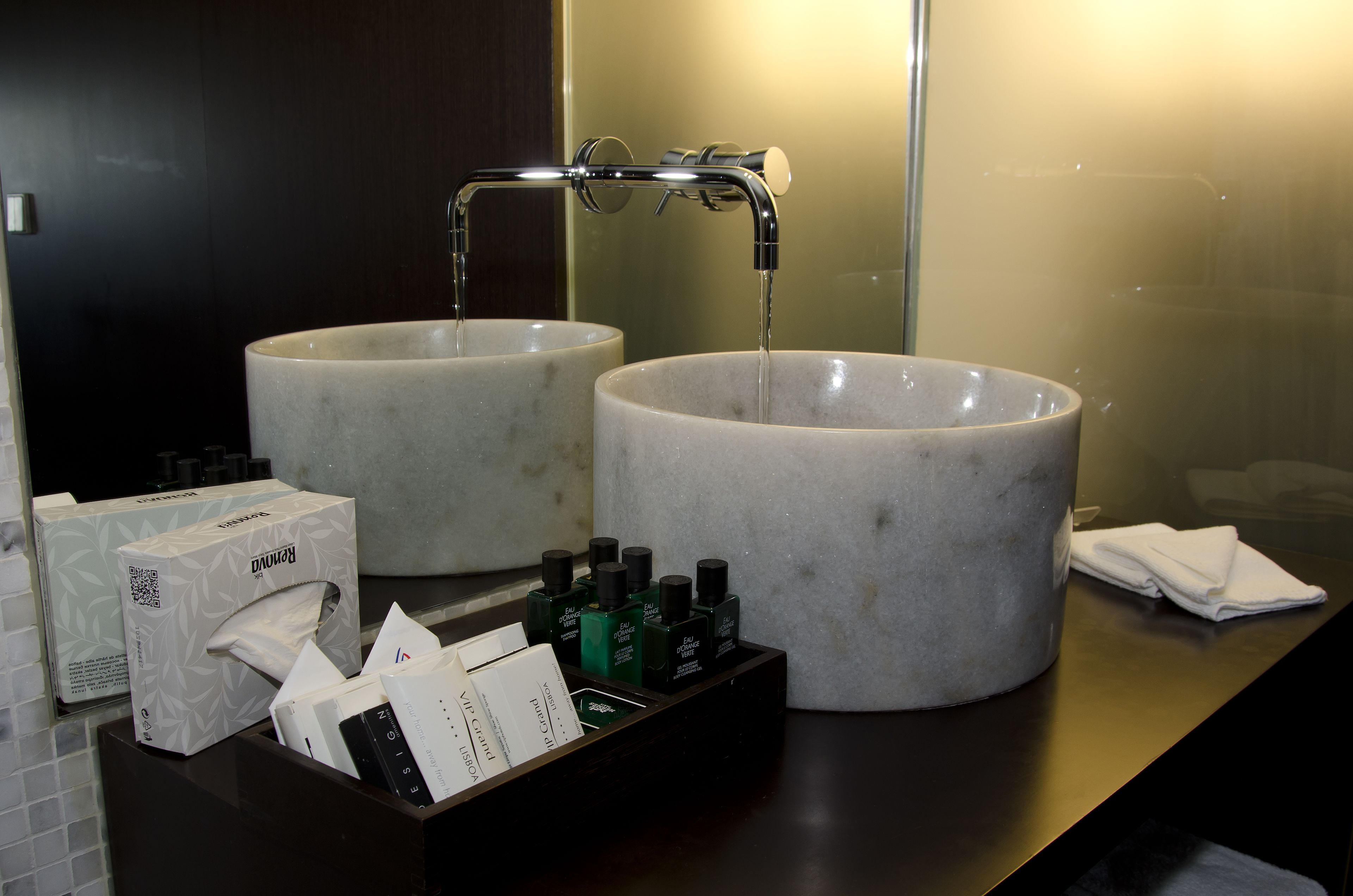Un bagno con due ampi lavabi in marmo, uno specchio e un piano d'appoggio nero con prodotti per l'igiene personale e una scatola di fazzoletti.