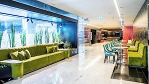A modern lobby with a green sofa, teal chairs, and a glass wall with plants. - VIP Grand Lisboa Hotel & Spa (Lisbon)
