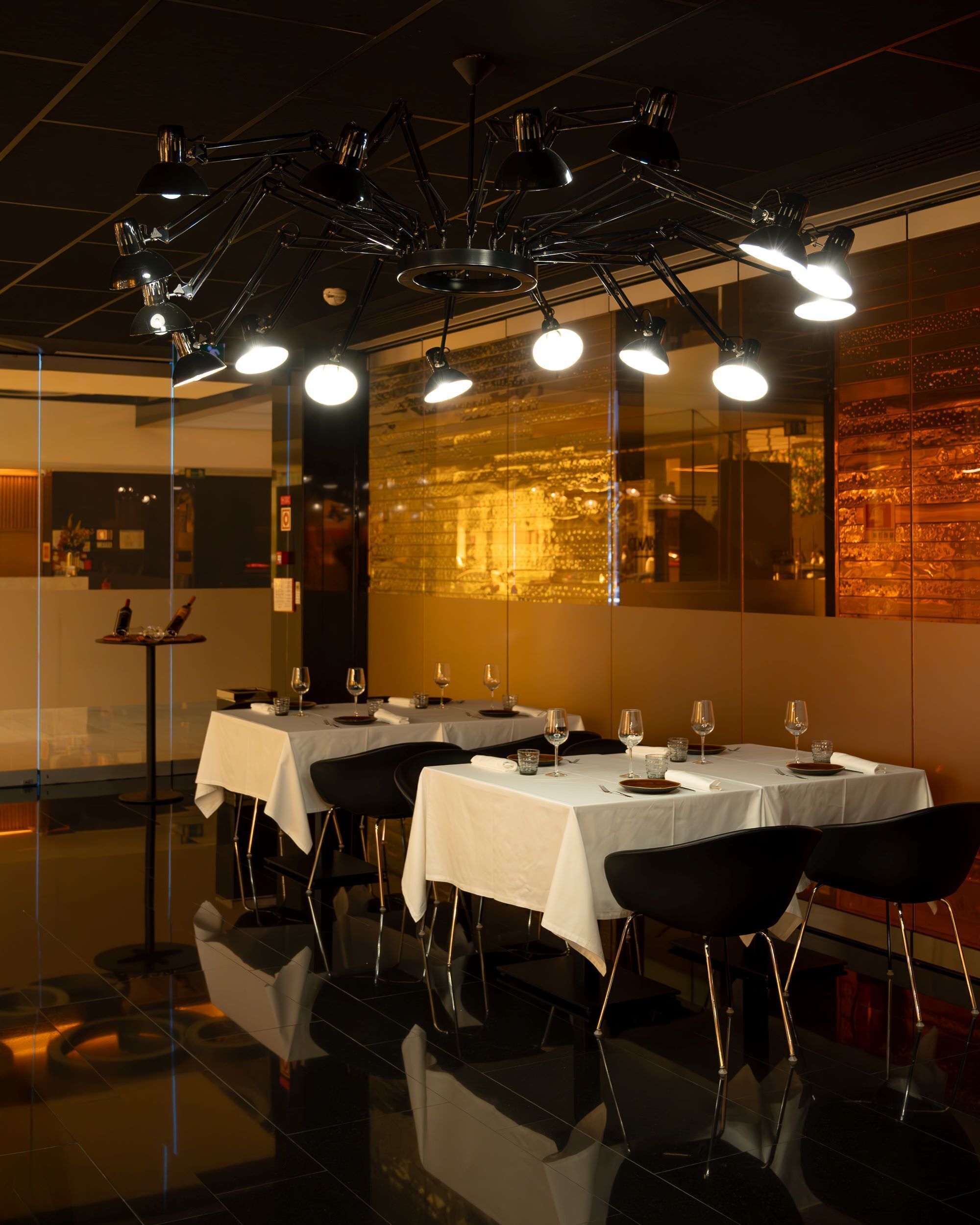 A restaurant with tables set for dining, overhead lighting, and a reflective floor.