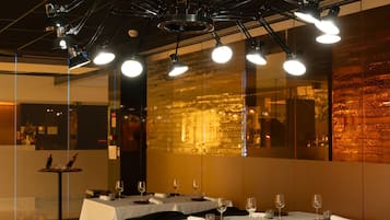 A restaurant with tables set for dining, overhead lighting, and a reflective floor.