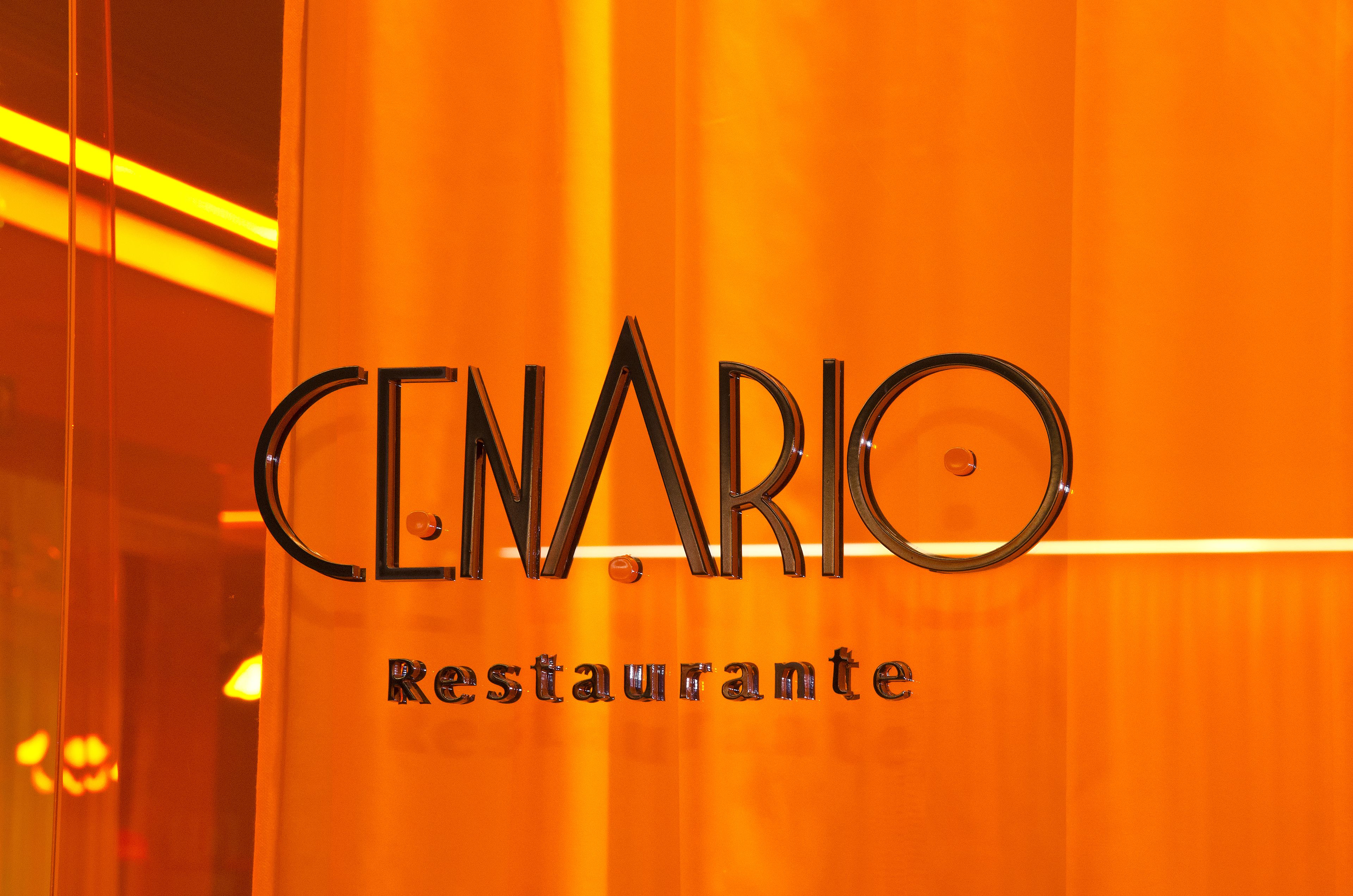 A sign with the words "CENARIO Restaurante" in a modern font, mounted on a glass door with an orange background.