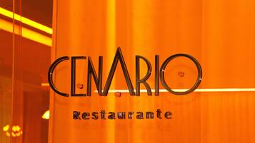 A sign with the words "CENARIO Restaurante" in a modern font, mounted on a glass door with an orange background.