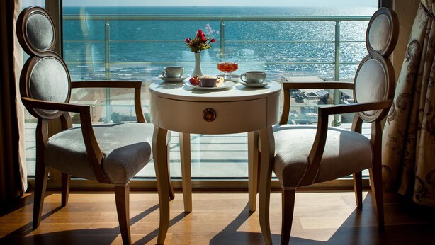 Una habitación con un ventanal grande que da al mar, una mesa redonda con un florero y dos sillas.