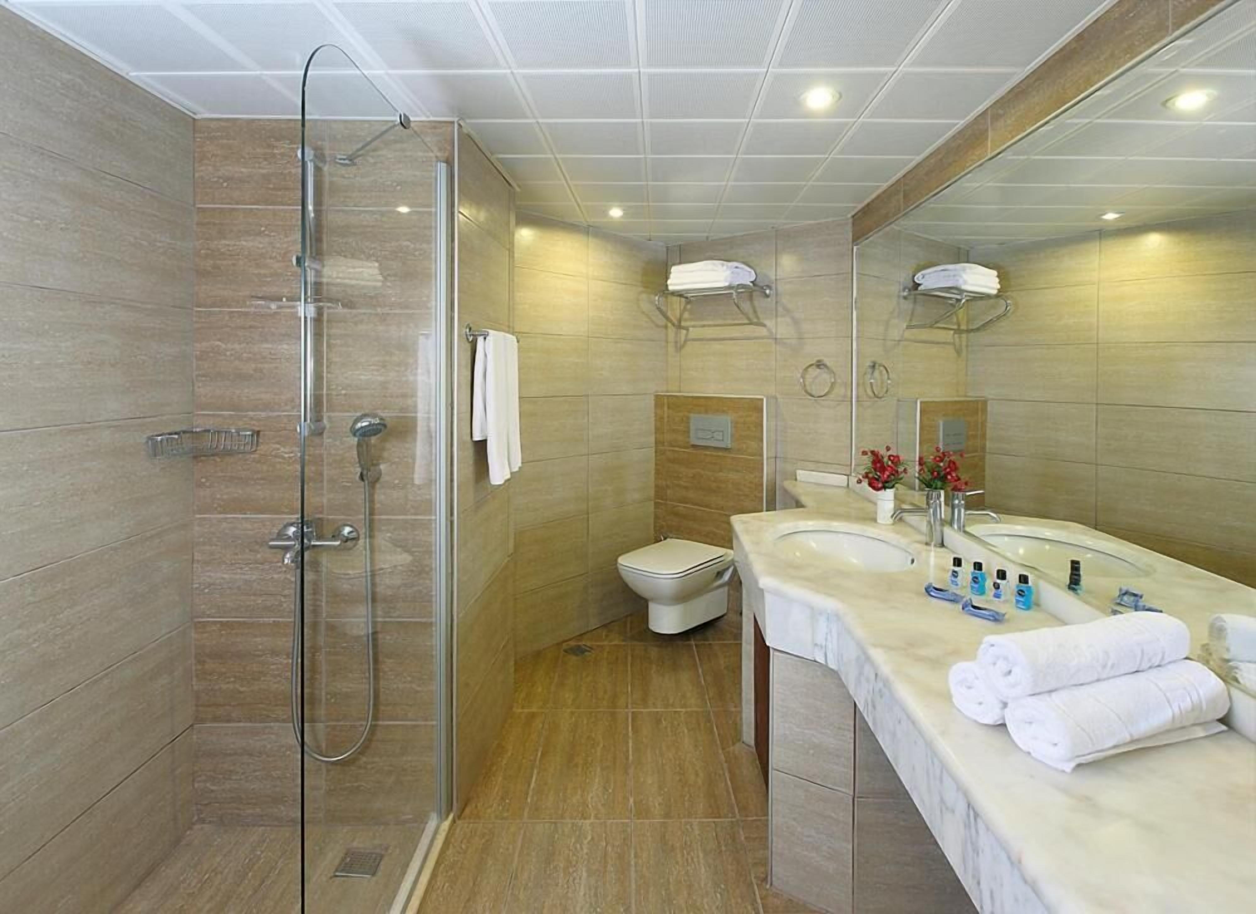Un baño moderno con ducha envuelta en vidrio, inodoro y tocador con lavamanos y barra para toallas.