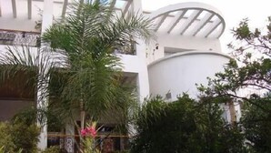 Un edificio moderno con fachada blanca curvada, una gran estructura cilíndrica y un balcón con barandillas de metal.