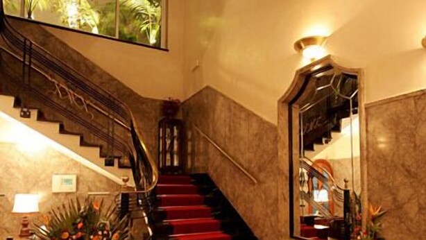 Un amplio vestíbulo con una escalera de mármol, asientos con alfombra roja y un espejo grande que refleja el interior.