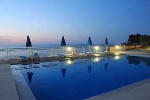 Una piscina con sillas de descanso y sombrillas, un flotador salvavidas y vistas al mar al atardecer.