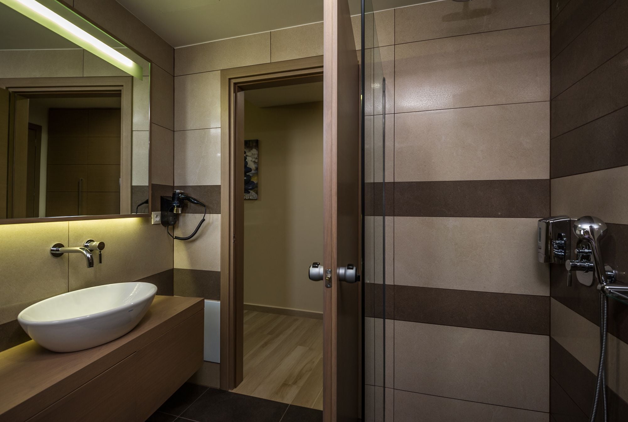 A modern bathroom with a glass shower enclosure, a white sink, and a mirror with a green light strip.