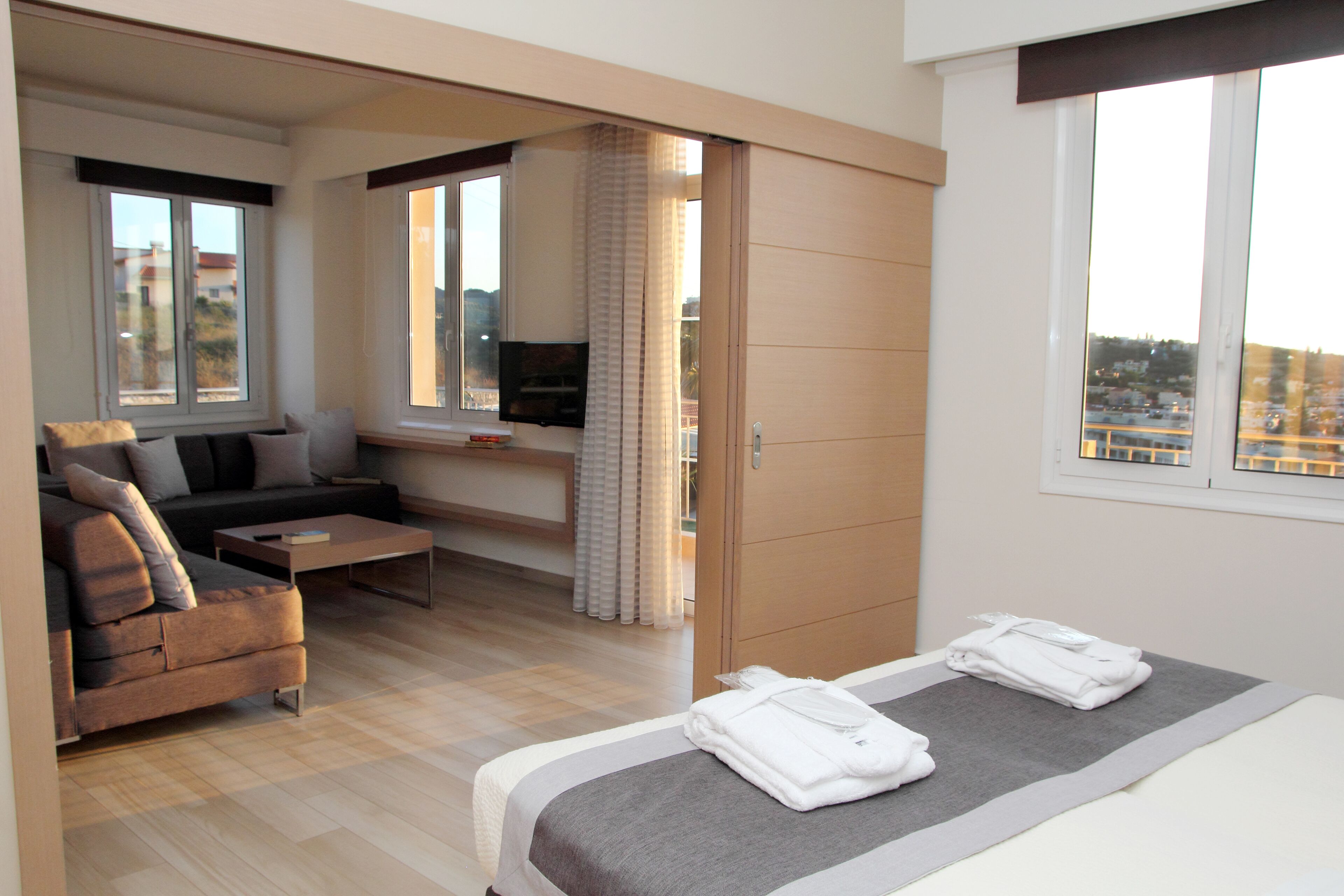 Een moderne hotelkamer met een bed, een bank, een televisie en uitzicht over de stad.