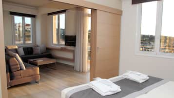 A modern hotel room with a bed, a sofa, a TV, and a city view.