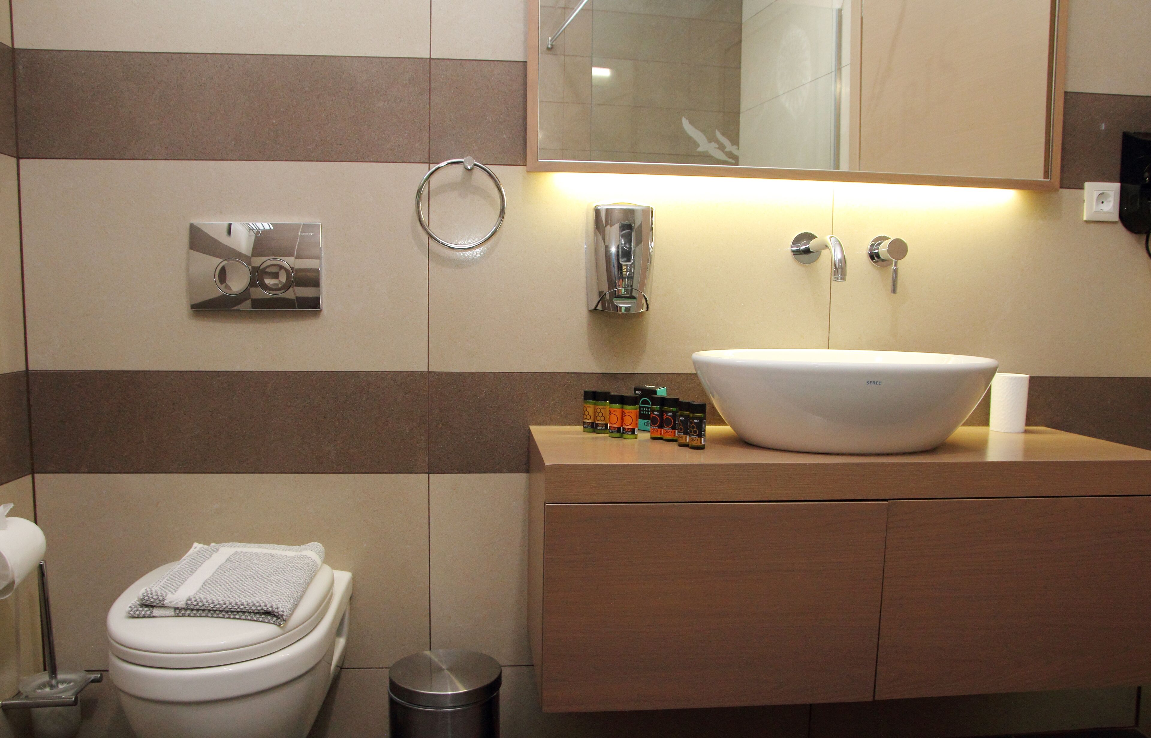 A modern bathroom with a large sink, a toilet, a hand dryer, and a mirror.