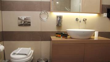 Un baño moderno con un lavamanos grande, un inodoro, un secador de manos y un espejo.