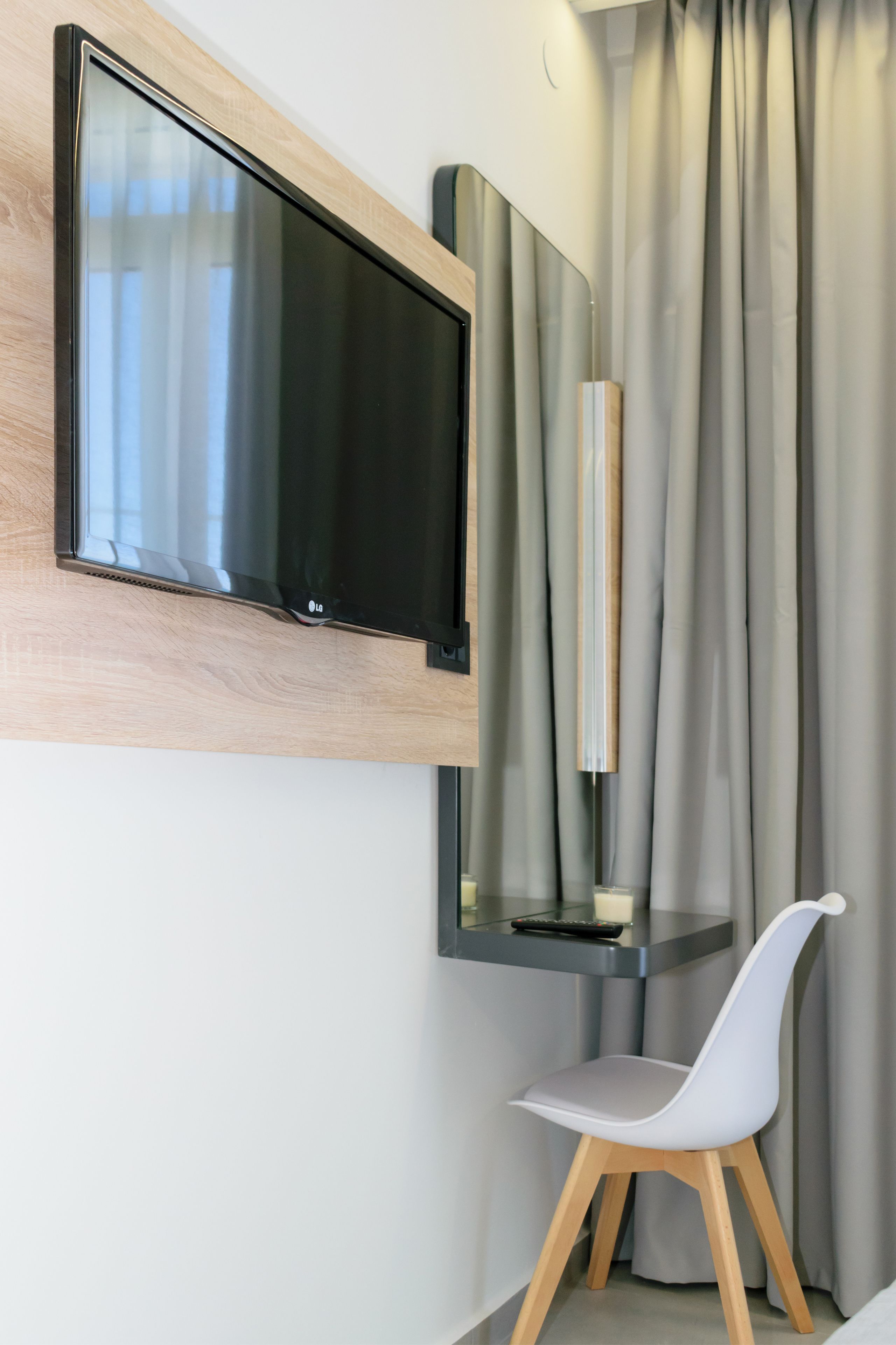 Una habitación moderna con una televisión de pantalla plana montada, una silla blanca y una cortina.