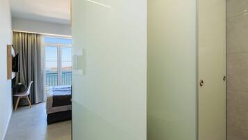 Habitació d'hotel moderna amb un llit, una taula de treball i una cadira. Hi ha una finestra gran amb cortines, i una porta que dona a una altra habitació.