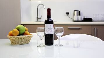 A bottle of wine, two glasses, and a basket of fruit on a table in a modern kitchen.