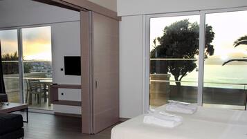Una habitación de hotel moderna con una cama grande, televisión, balcón con vista al mar y zona de comedor.