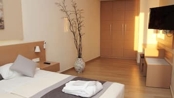 Una habitación de hotel con cama, mesita de noche, lámpara, jarra con ramas, armario y televisor.