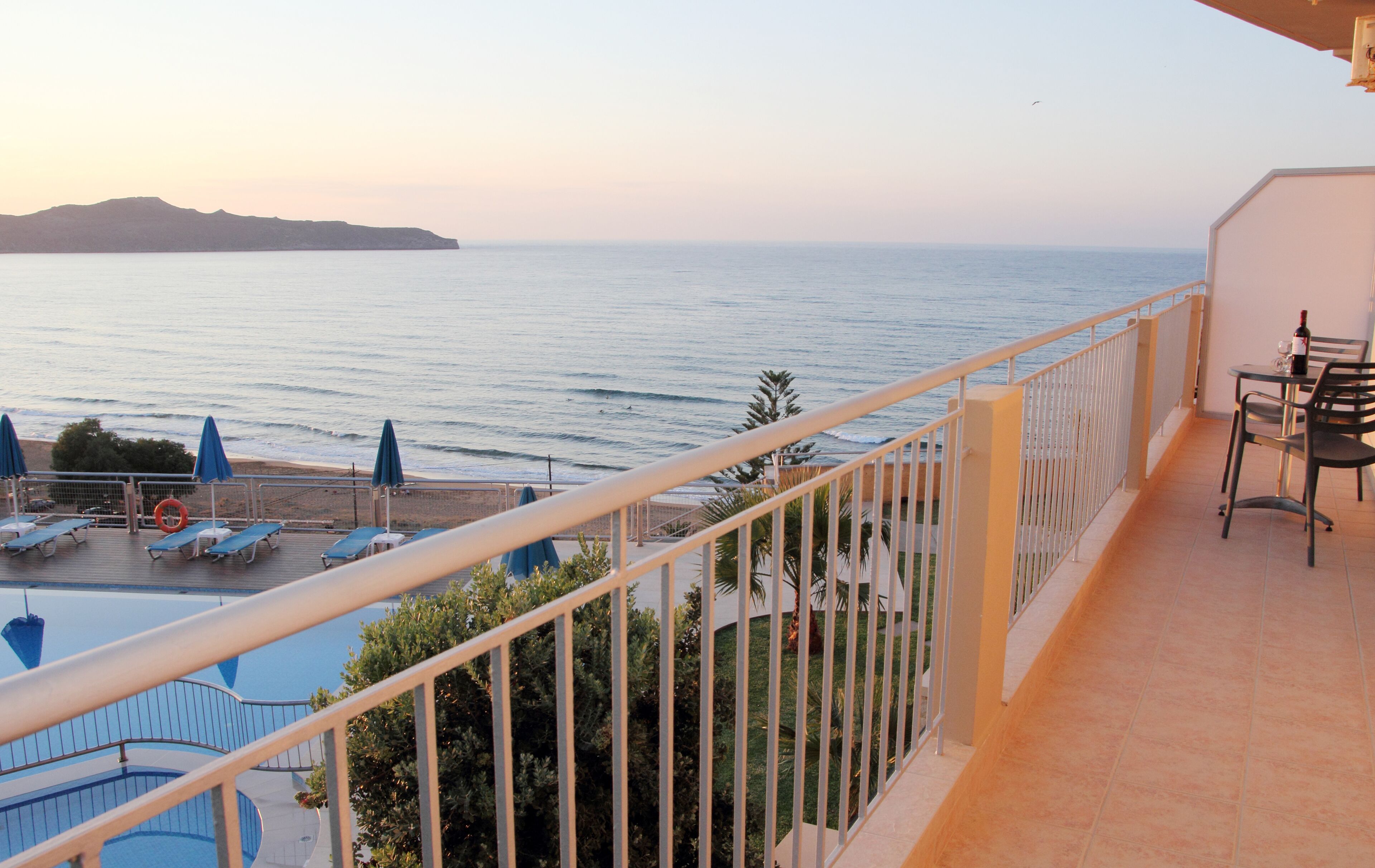 A balcony with a view of the sea, a table with chairs, and sun loungers.