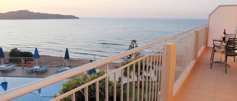 A balcony with a view of the sea, a table with chairs, and sun loungers.