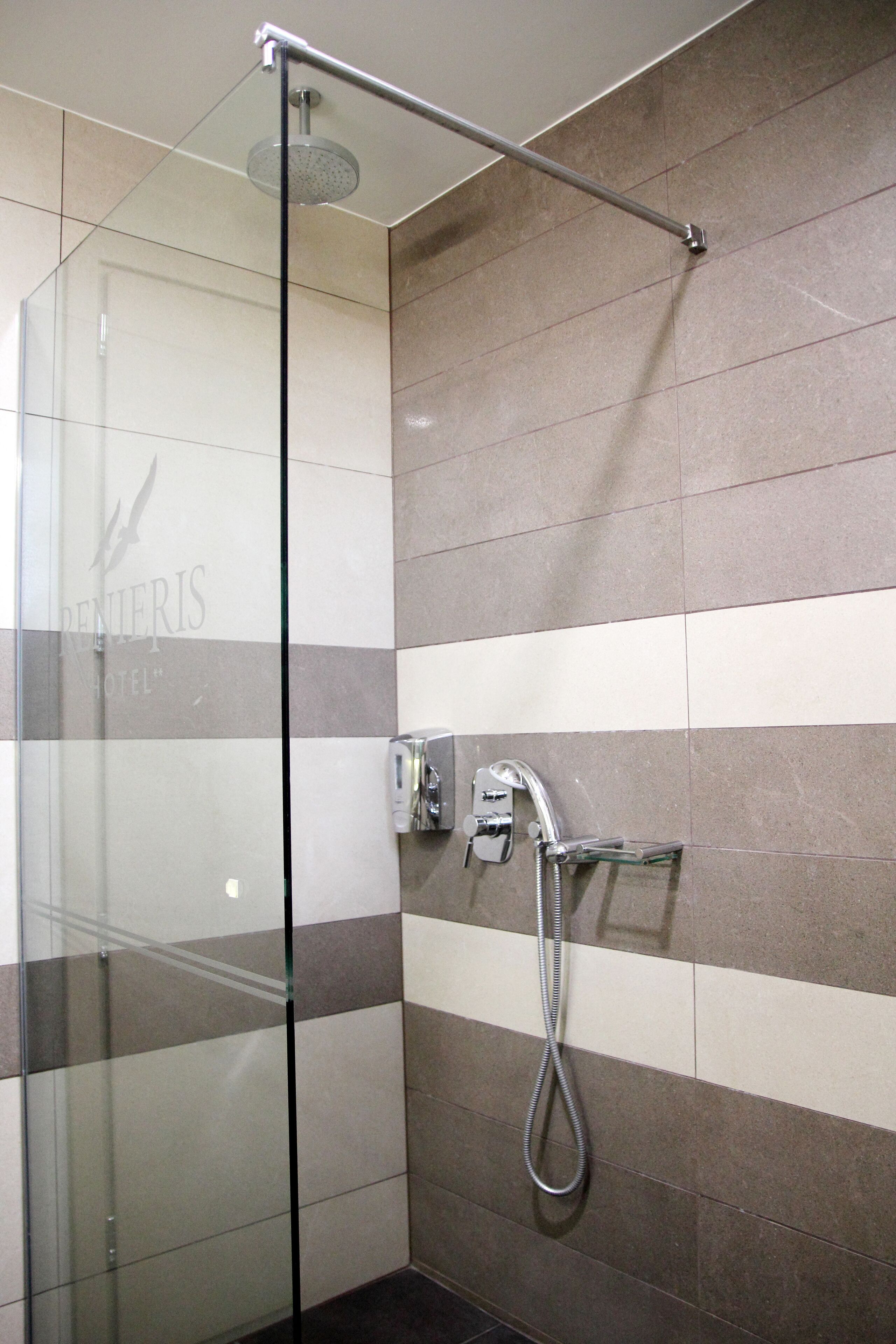 A glass-enclosed shower area with a handheld showerhead and a wall-mounted faucet.