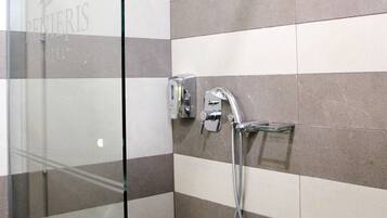 A glass-enclosed shower area with a handheld showerhead and a wall-mounted faucet.