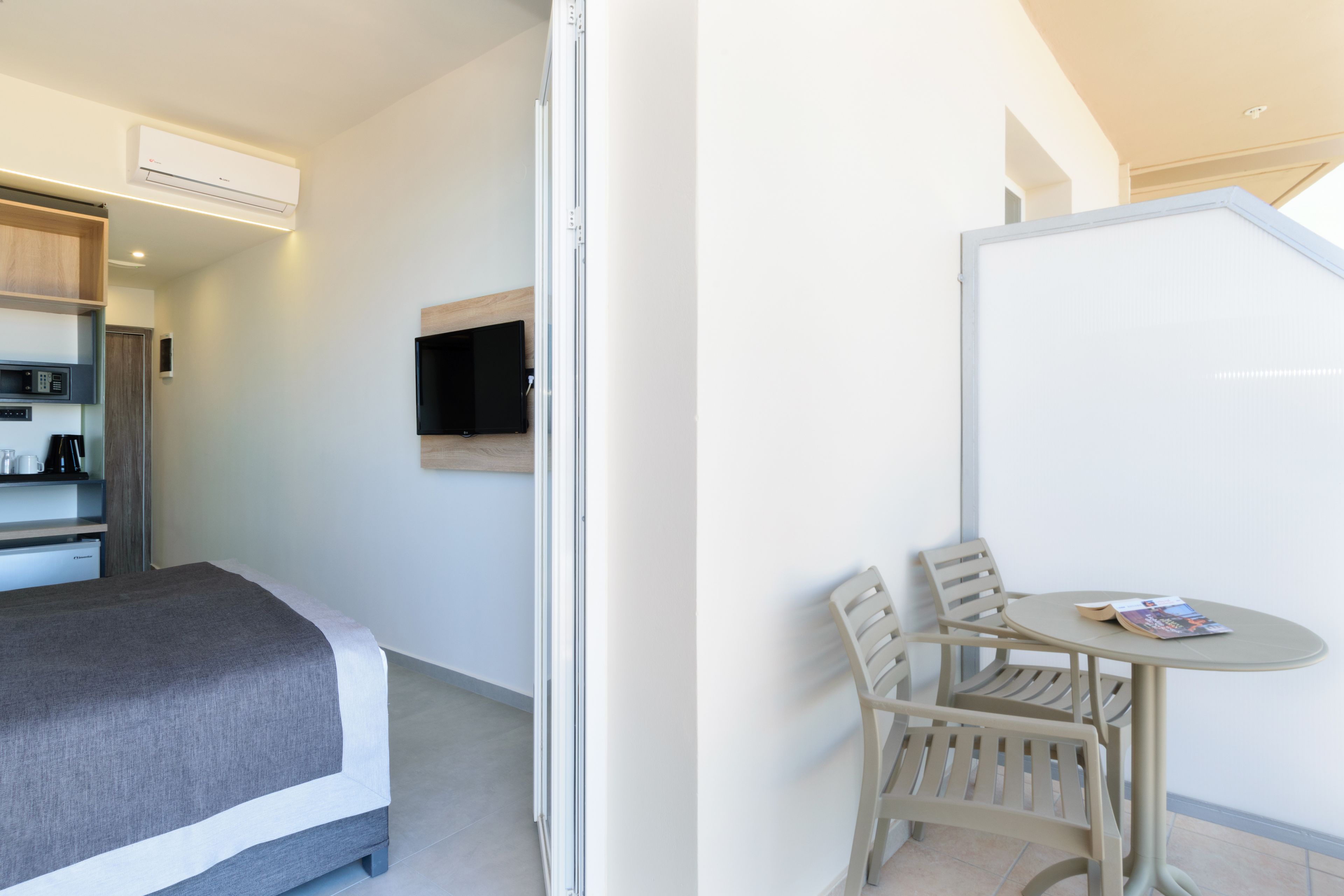 A hotel room with a bed, a small table with chairs, a TV mounted on the wall, and a kitchenette area.