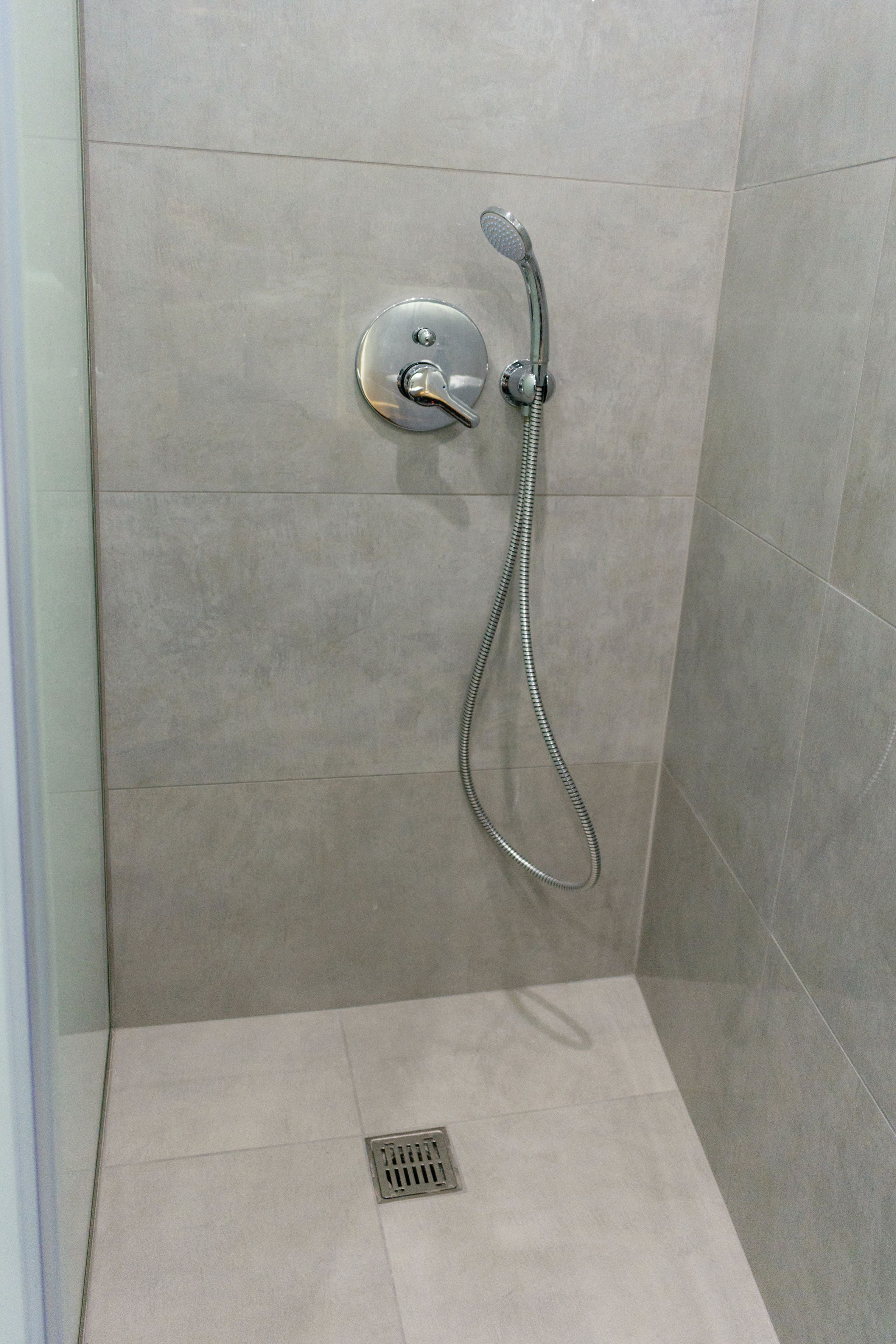 A shower with a handheld showerhead and a wall-mounted control.