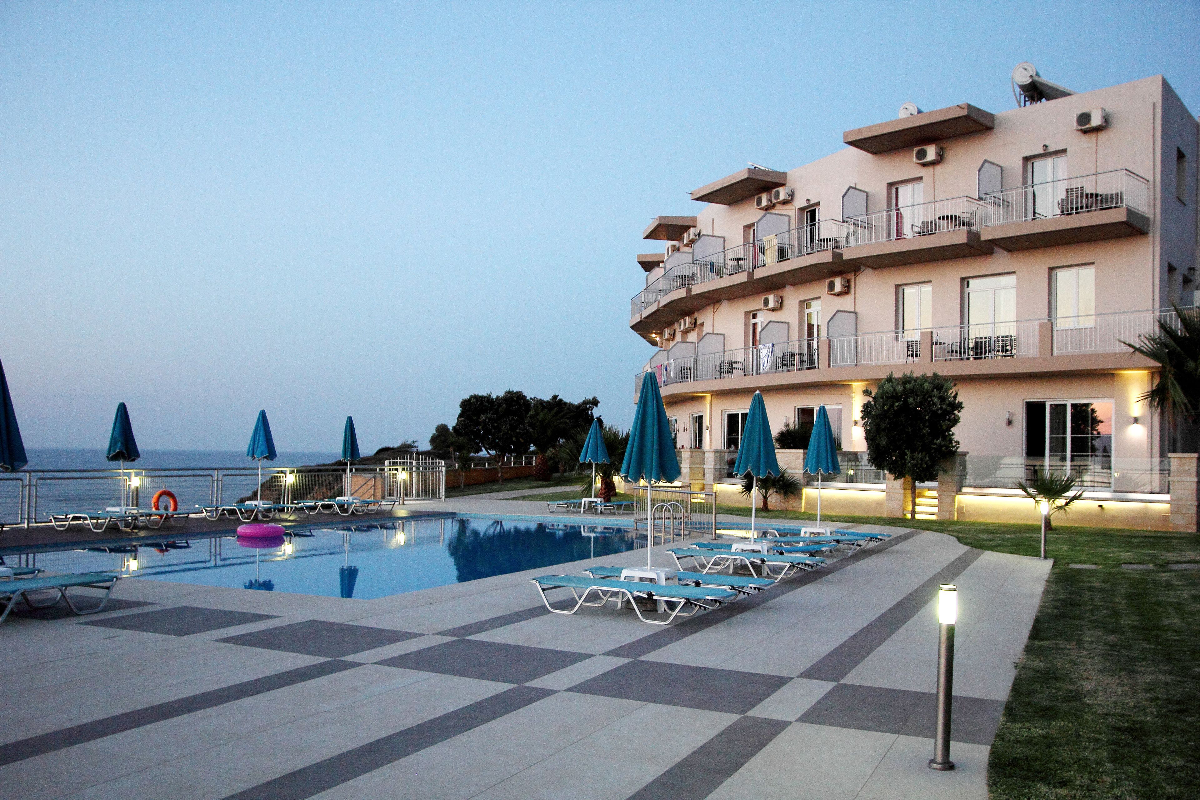 A hotel with a swimming pool, lounge chairs, and umbrellas.