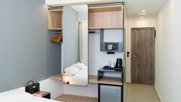 Habitación de hotel pequeña y funcional, con cama, escritorio, espejo, minibar y armario.