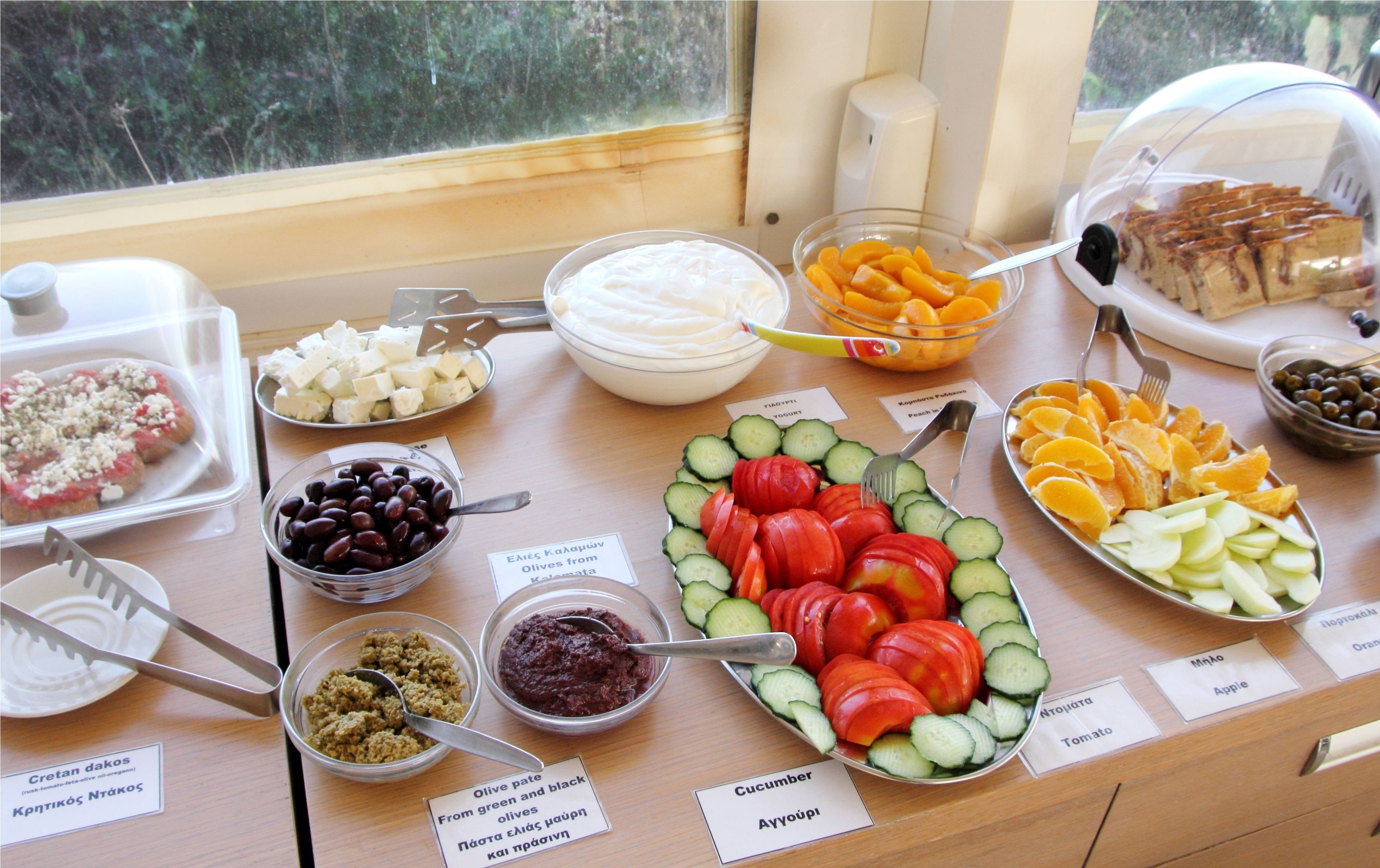 Una mesa de buffet con diversos alimentos y etiquetas que indican sus nombres.