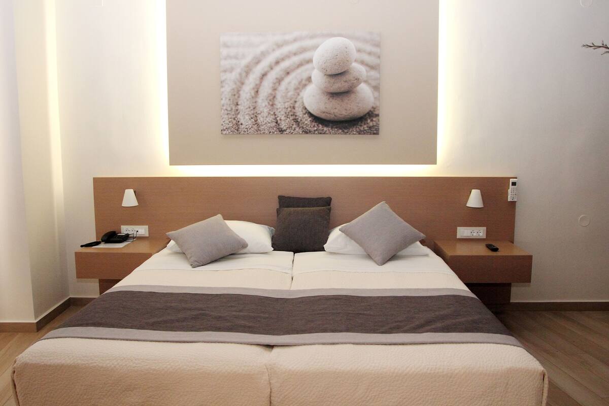 Ein Hotelzimmer mit einem Bett, Nachttischen, einem Telefon, einer Fernbedienung und einem Wandbild.