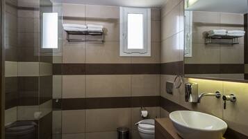 A modern bathroom with a glass shower enclosure, a toilet, a bidet, a sink with a large basin, and a towel rack with towels.