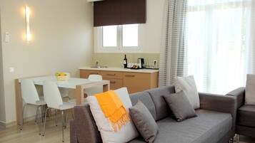 A modern living room with a grey sofa, white chairs, a dining table, and a kitchen area with a window above the counter.