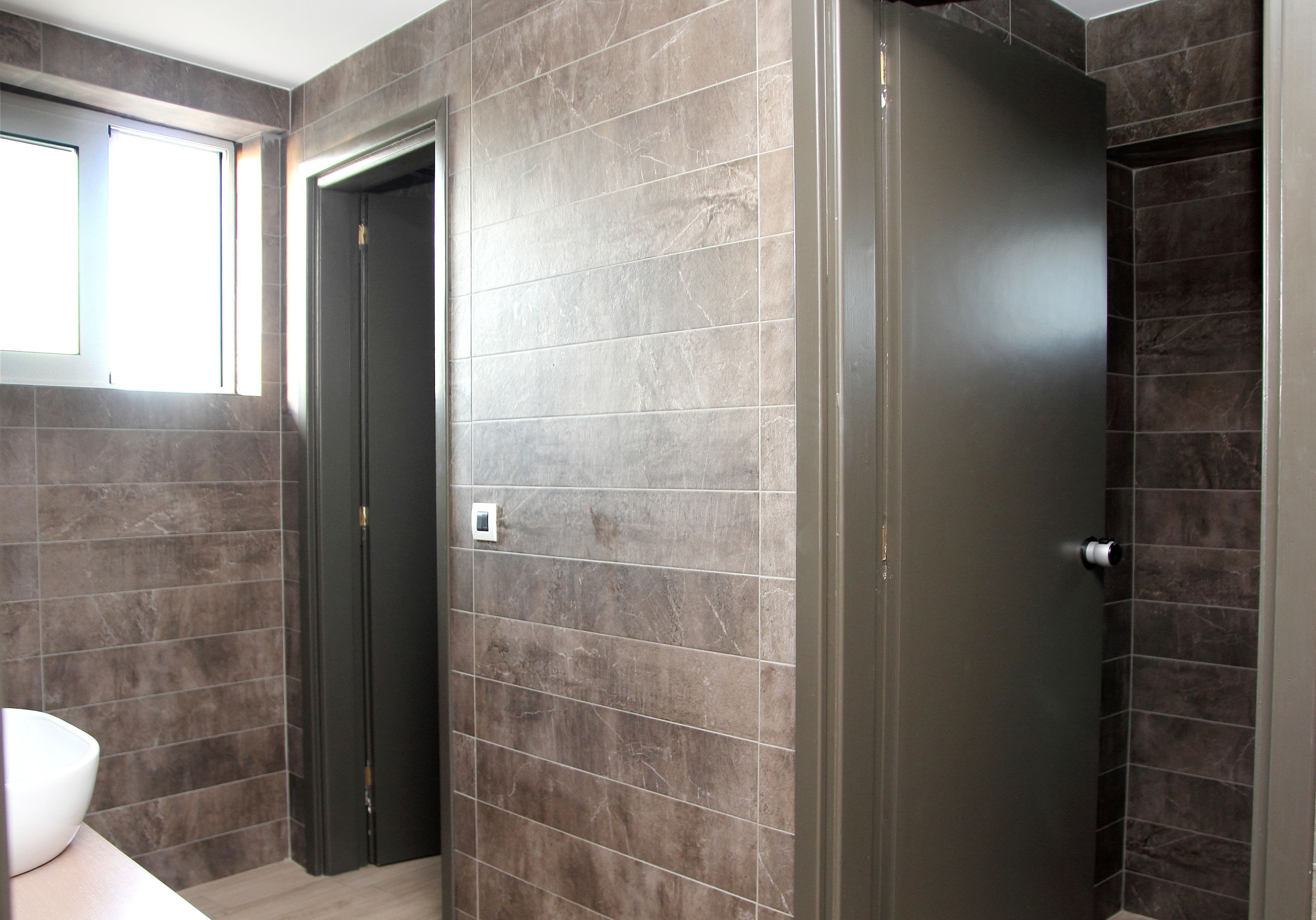 A modern bathroom with dark tiled walls, a white sink, and a door leading to another room.