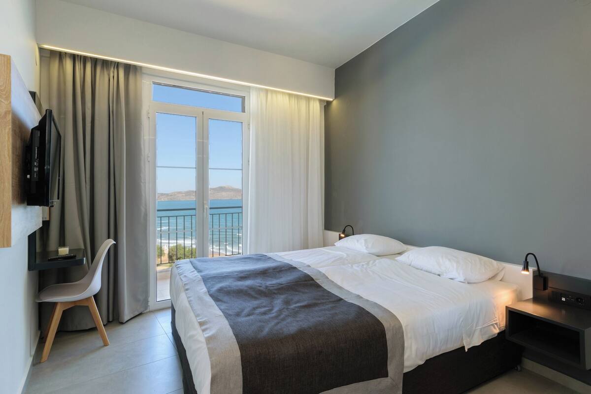 Ein modernes Hotelzimmer mit Bett, Schreibtisch, Stuhl, Fernseher und einem Balkon mit Blick.