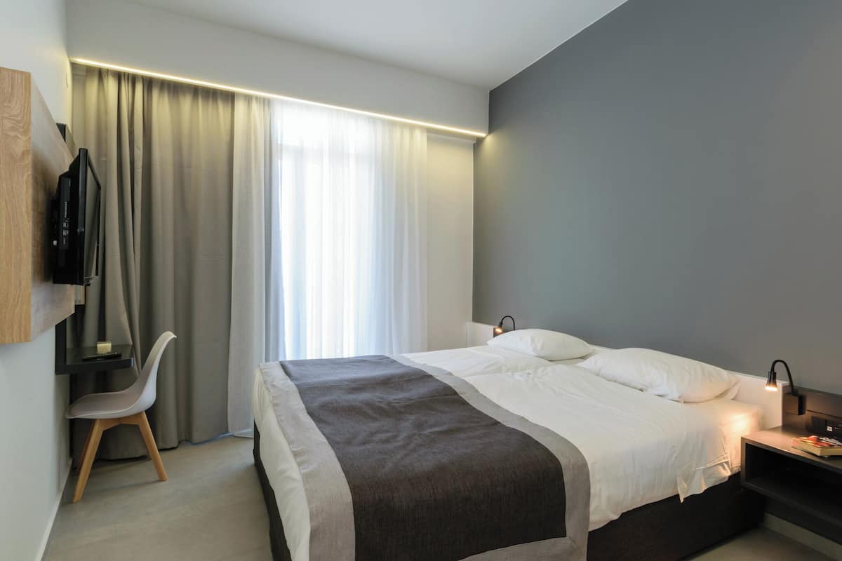 Ein modernes Hotelzimmer mit Bett, Schreibtisch, Stuhl und Fernseher.