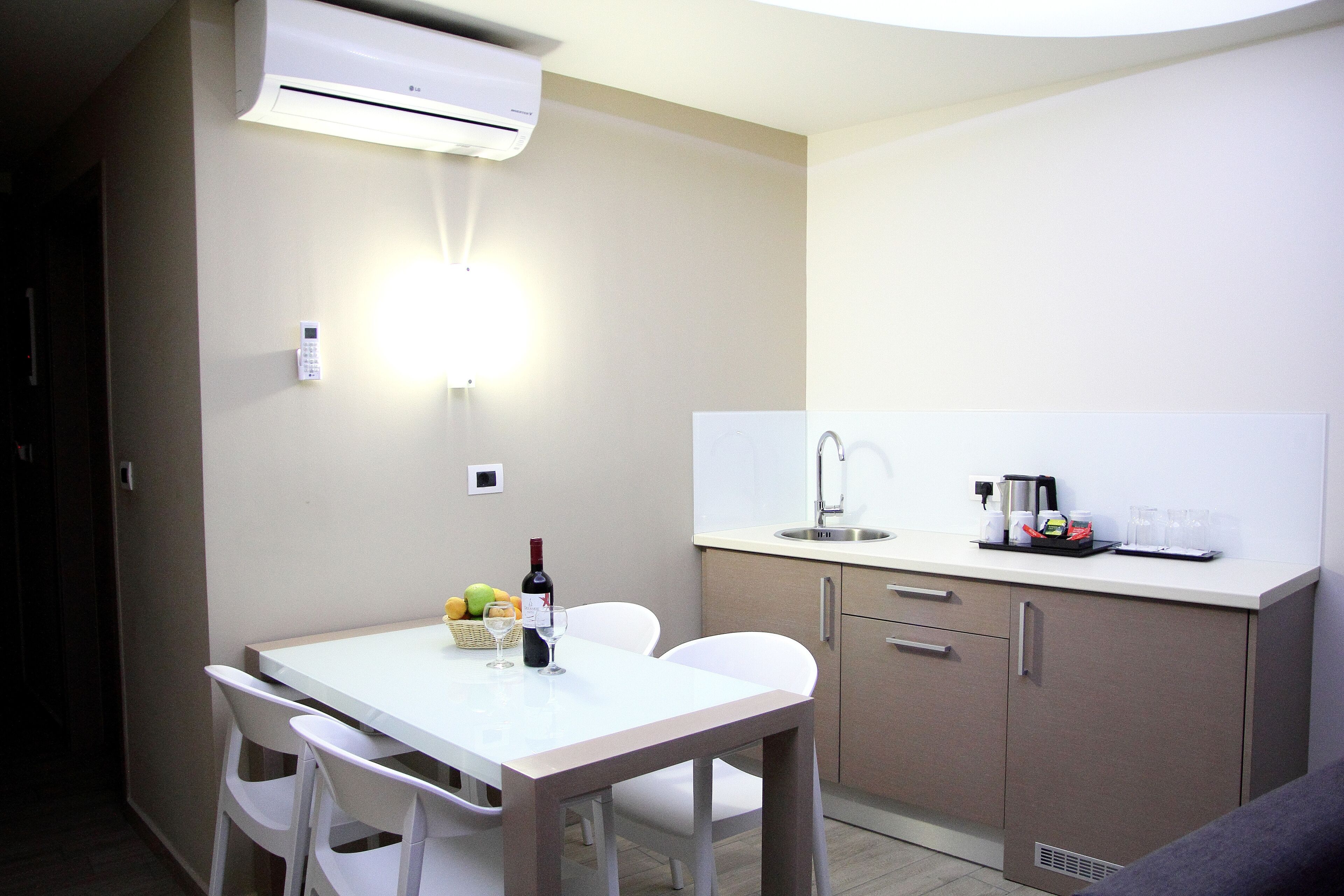 Cocina compacta con mesa blanca, sillas, un lavamanos y una encimera con cafetera y cristalería.