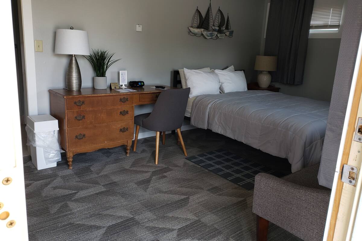 A bedroom with a bed, a desk with a computer, a chair, a dresser, and a wall-mounted decoration.