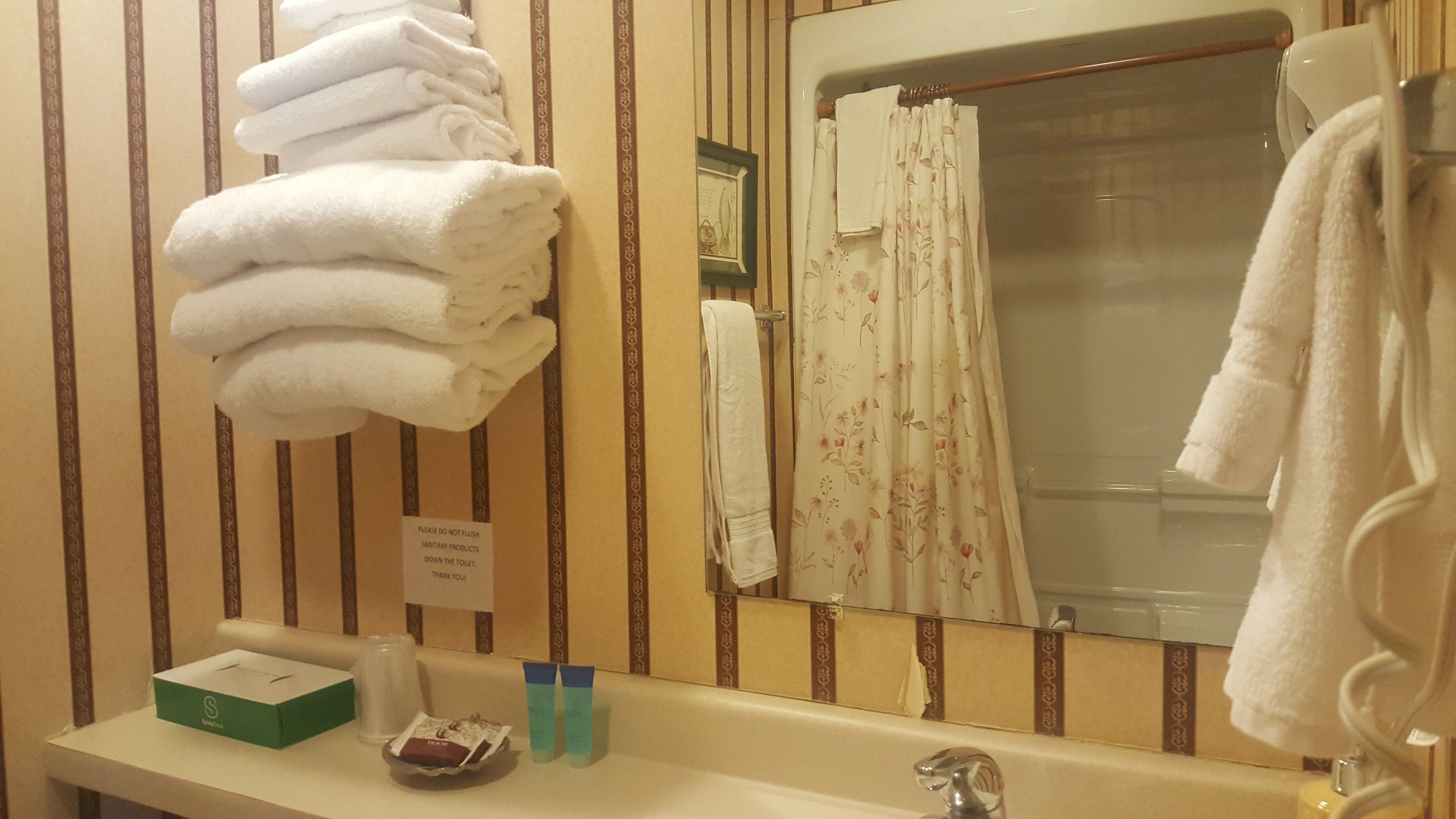 Un baño con paredes a rayas, un lavamanos con artículos de aseo, un toallero con toallas dobladas y una cortina de ducha.