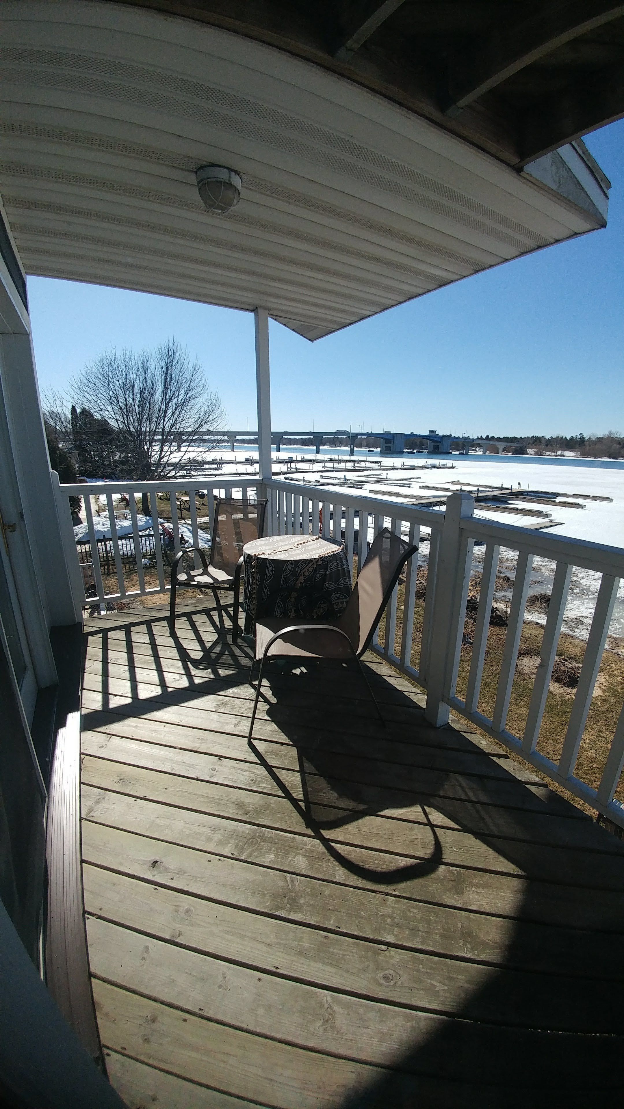 A wooden deck with a table and chairs, a white railing, and a view of a frozen body of water.