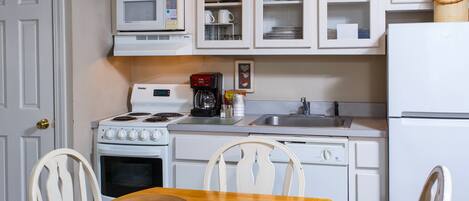 A kitchen with white cabinets, a microwave, a stove, a sink, and a refrigerator. There is a wooden table with two chairs.