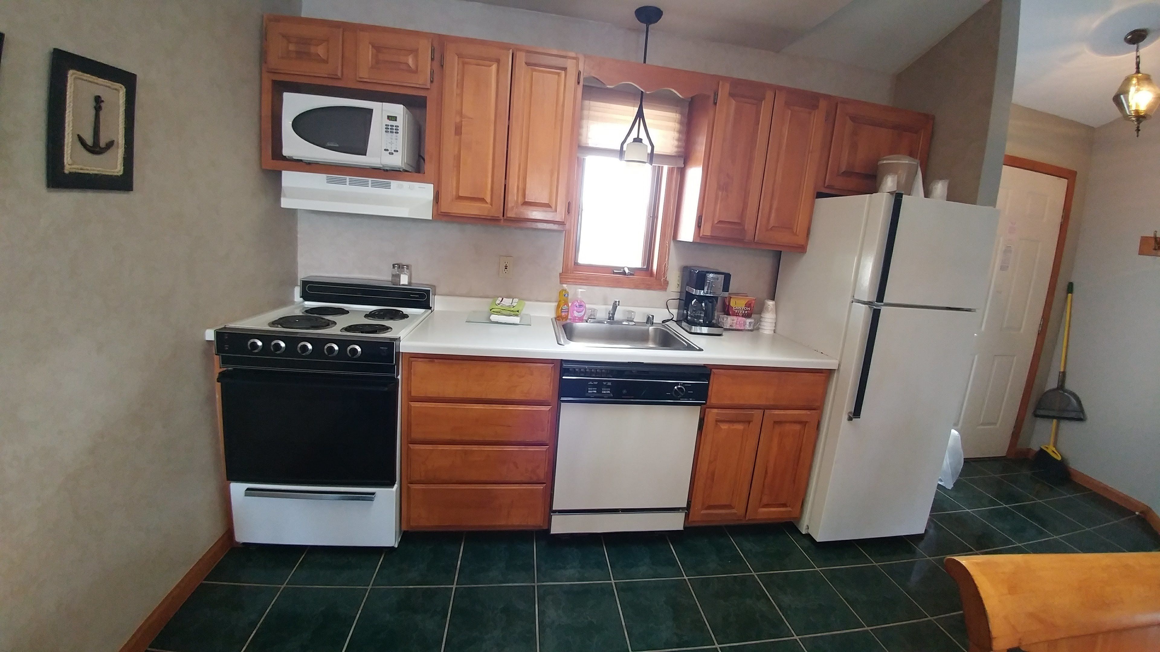 Cocina compacta con armarios de madera, microondas, estufa, lavavajillas y refrigerador.