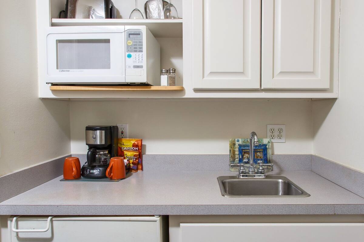A compact kitchen with a microwave, coffee maker, and orange mugs on the counter.
