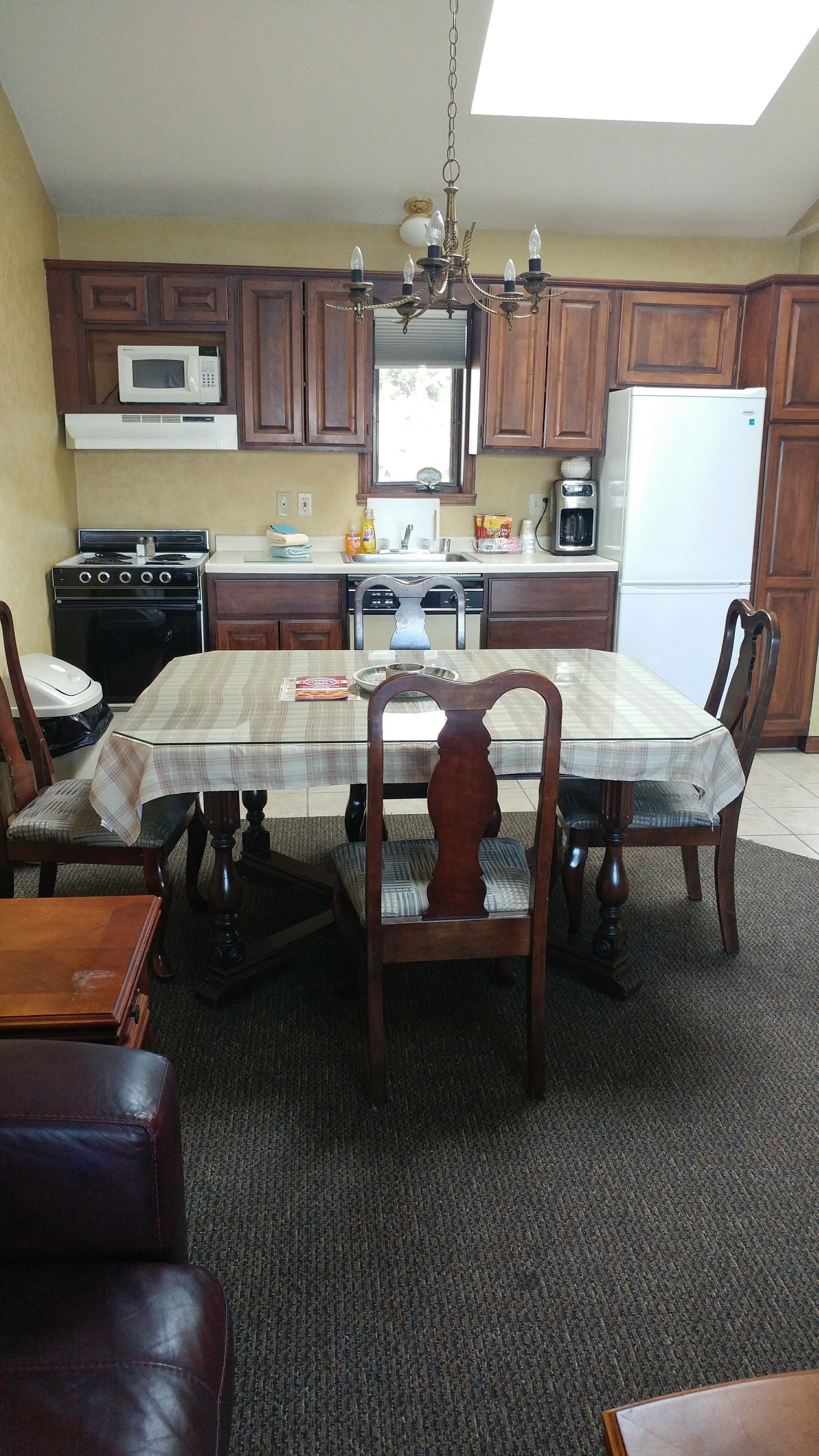 A kitchen with wooden cabinets, a microwave, stove, and a refrigerator. There is a dining table with chairs and a chandelier.